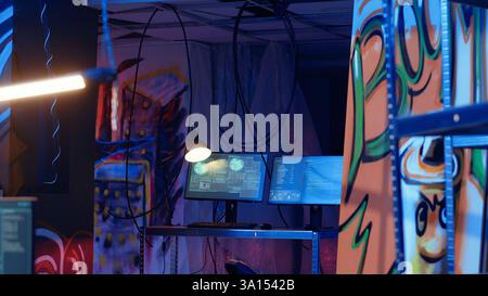 Software interface on computer screens showing developer code running in empty criminals den with graffiti sprayed on walls. Hacking malware programming in underground base Stock Photo
