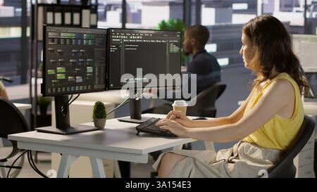 Manager in wheelchair passing by desk of employee testing machine learning company software to minimize occurrence of bugs. Woman works in inclusive workspace with workers with disabilities, camera A Stock Photo