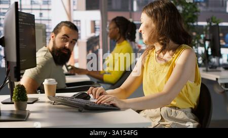 Man with paraplegia drinking coffee, checking progress done by employee doing code review to fix bugs. Worker code, being supervised by manager in wheelchair enjoying beverage, camera A Stock Photo