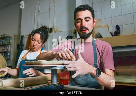 Potter explaining clay work to his female apprentice in a pottery workshop Stock Photo