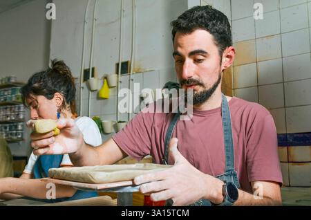 Craftsman shaping clay on a slab roller in pottery studio, working with raw materials and traditional techniques Stock Photo