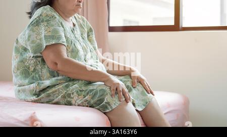 Cropped shot of senior woman suffering from pain in knees at home. Holding her knee and massaging with hands, feeling exhausted. Stock Photo