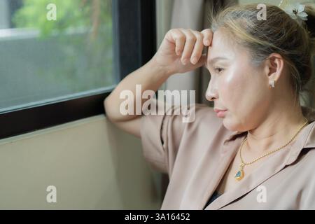 Asian woman covering her face feeling sorrow and depressed sit nearby the window while looking outside. Copy space. Stock Photo