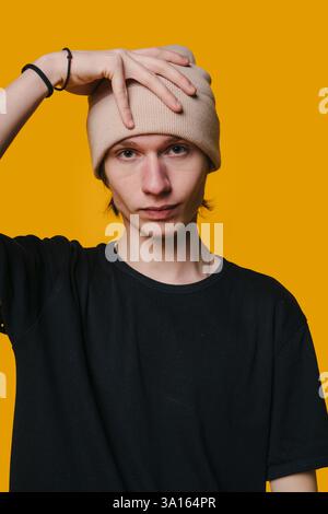 A stylish young man in a beanie stands confidently against a bright yellow background Stock Photo