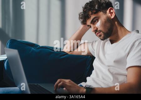 A Thoughtful and Pensive Young Man Engaged in Working on His Laptop at Home Comfortably Stock Photo