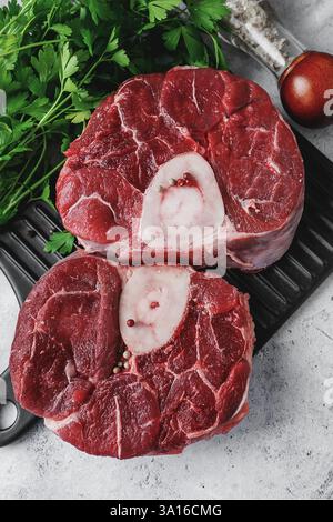 Two pieces of raw osabuko beef shank lie on a smooth black cutting board surrounded by fresh parsley greens, showing off their deep red colour and att Stock Photo