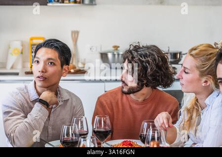Group of diverse friends engaging in a captivating conversation while enjoying a meal together in a modern kitchen Stock Photo