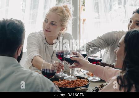Group of friends toasting red wine glasses while having lunch together at home Stock Photo