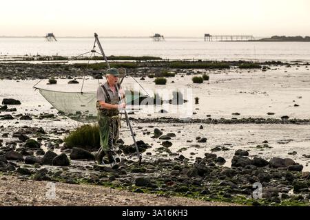 France, Charente Maritime, Port-des-Barques, hand net fisherman and huts on stilts called carrelets in the background Stock Photo