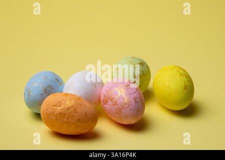 Colorful easter eggs with a cracked paint finish and gold accents are displayed against a bright yellow backdrop in a studio setting. Stock Photo