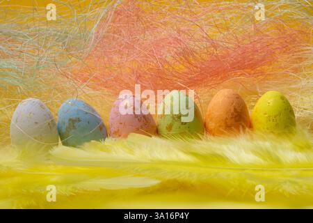 Six gold-touched Easter eggs line soft yellow feathers against a bright yellow backdrop. Stock Photo