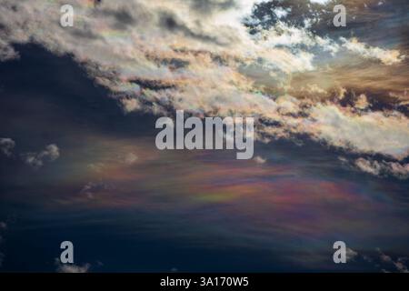 Sky photo featuring a mesmerizing pearl cloud beneath white clouds, with the sun hidden behind them. The intense light creates an abstract painting Stock Photo