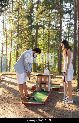 Young adult couple playing mini golf on outside court in forest Stock Photo