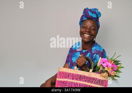 Smiling woman holding pink woven bag and colorful flowers Stock Photo