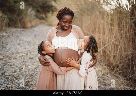 Happy smiling mix race girls hugging black pregnant mom belly Stock Photo