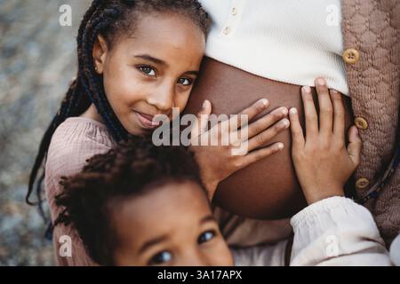 Black pregnant mother and mix race kids touching belly Stock Photo