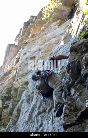 A rock climber ascends a steep cliff using ropes and climbing gear ...