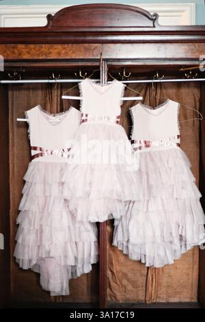 Three ruffled pink flower girl dresses hanging in a vintage war Stock Photo