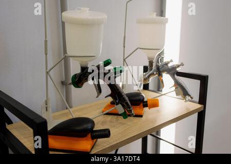 In a stylish workspace filled with light, two spray guns are set on a wooden shelf, ready for vibrant painting sessions. The tools, complete with pain Stock Photo