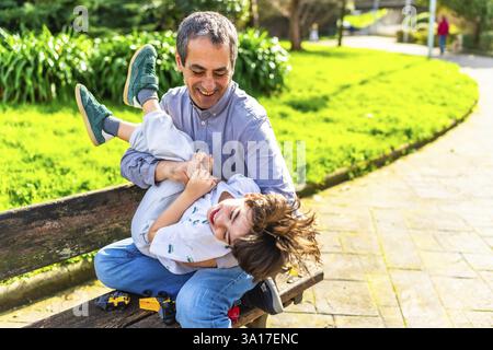 Grandfather and grandson laughing and playing together on a park bench, enjoying quality time outdoors Stock Photo