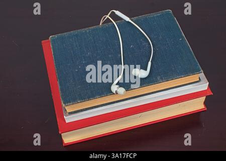 A pair of white earphones sitting on top of a stack of books. This shows the contrast between traditional print books and the ability to use Stock Photo