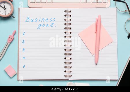 Open notebook with text BUSINESS GOAL,  pen and sticky paper on blue background. Top view Stock Photo