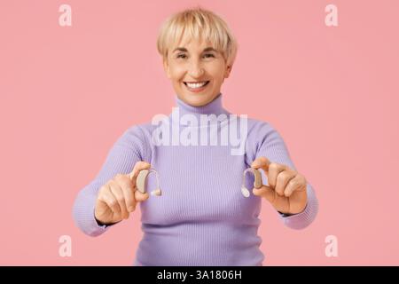 Mature woman with hearing aids on  pink background Stock Photo