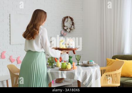 Beautiful woman serving table for Easter celebration in dining room Stock Photo