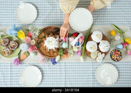 Female hands holding plate and putting egg on table setting for Easter celebration. Top view Stock Photo