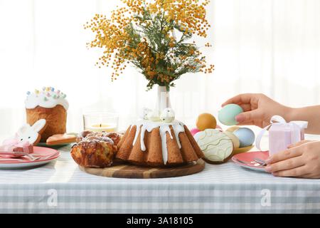 Female hands with painted egg and gift box at table setting for Easter celebration in room. Closeup Stock Photo