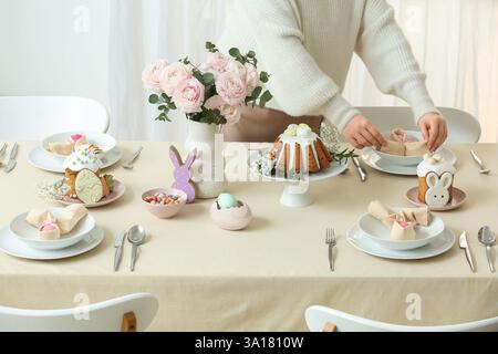 Woman decorating festive Easter table setting with painted egg in napkin in room. Closeup Stock Photo