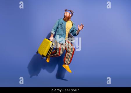 Energetic man with red hair and a beard happily jumps in colorful attire against a vibrant purple background Stock Photo