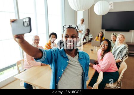 A group of smiling business colleagues from diverse backgrounds taking a joyful selfie during an office meeting. The image showcases teamwork, diversi Stock Photo