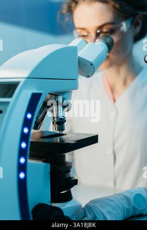 A young female scientist conducts research in a medical lab, using a microscope. The concept of precise scientific experiments to discover new medical Stock Photo