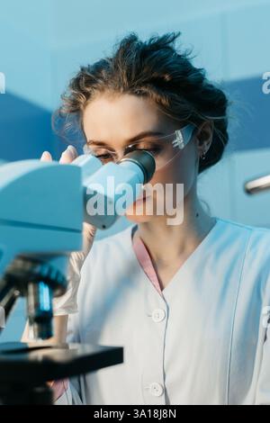 A young female scientist conducts research in a medical lab, using a microscope. The concept of precise scientific experiments to discover new medical Stock Photo