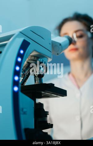A young female scientist conducts research in a medical lab, using a microscope. The concept of precise scientific experiments to discover new medical Stock Photo