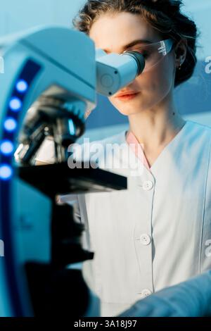 A young female scientist conducts research in a medical lab, using a microscope. The concept of precise scientific experiments to discover new medical Stock Photo