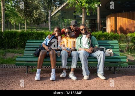 Happy young couples, black men and women, sit on park bench during double date, looking at camera Stock Photo