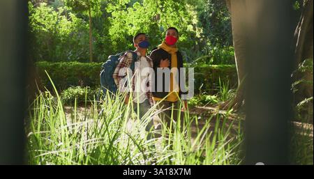 Two happy biracial male friends walking and talking in park with backpacks Stock Photo