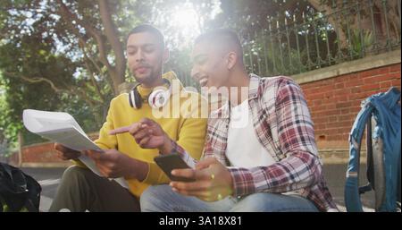 Two happy biracial male friends sitting, using smartphone and map Stock Photo