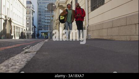 Two happy biracial male friends walking and talking in the street Stock Photo