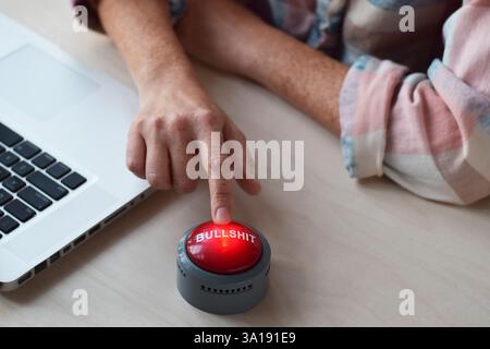 Closeup on woman's hand finger pressing red Bullshit button sitting at a desk Stock Photo
