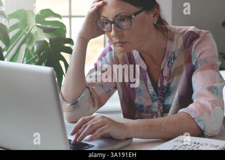 Middle aged woman sitting at desk using laptop computer looking serious and focused Stock Photo
