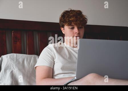 Young man sitting on bed using laptop computer Stock Photo