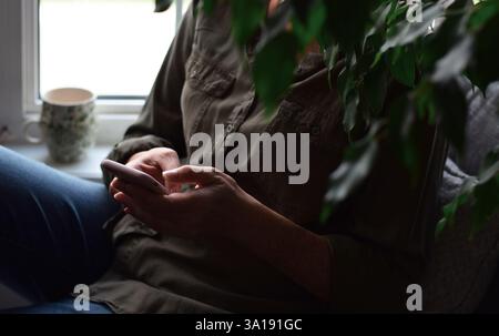 Woman sitting in cozy nook by a window at home using mobile phone Stock Photo