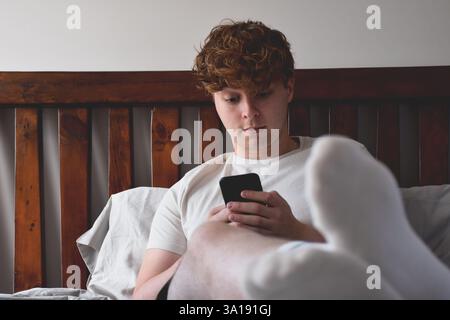 Young man sitting on bed using mobile phone Stock Photo