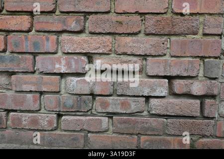 A brick wall with a few missing bricks. The wall is brown and has a rough texture. The missing bricks create a sense of disrepair and neglect Stock Photo