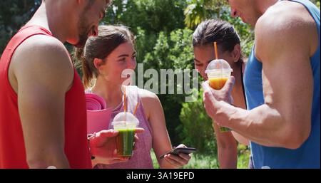 Happy diverse group of men and women using smartphone and talking after yoga class in sunny park Stock Photo