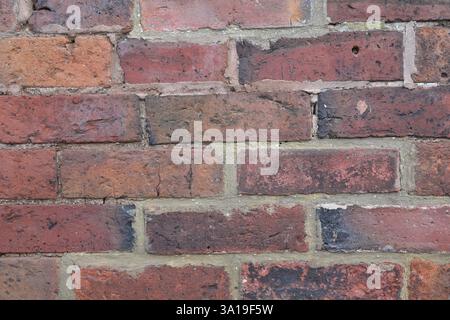 A brick wall with a few holes in it. The wall is made of red bricks and has a rough texture Stock Photo