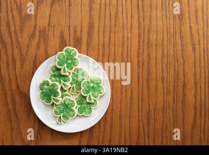 top down flat lay of green shamrock sugar cookies on white plate on wood table Stock Photo
